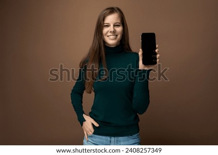 Smiling 30 year old woman with brown eyes showing smartphone screen mockup Royalty-Free Stock Photo #2408257349