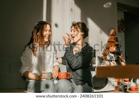 Cozy morning: girls friends talking over a cup of coffee in a bright kitchen Two women spend time peacefully on a sunny day with mugs of tea Royalty-Free Stock Photo #2408261101
