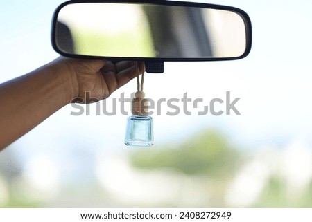 The female driver's hand puts the hanging car perfume on the rear view mirror of the car.  perfume packaged in bottles and wooden caps Royalty-Free Stock Photo #2408272949