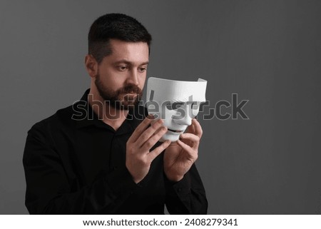 Multiple personality concept. Man putting on mask against grey background. Space for text