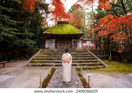 Kyoto, Japan. A woman wearing kimono in Honen-in Temple fall foliage garden. Maple trees turn red in autumn. Japanese traditional building and stone stairs in the background. Zen concept.