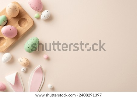 Easter sweetness captured from above. Traditional eggs in wooden holder, adorable bunny ears adorn a pastel beige background—perfect for your personalized text or promotional message Royalty-Free Stock Photo #2408291397