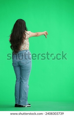 A woman, on a green background, in full height, shows her thumbs down, back view