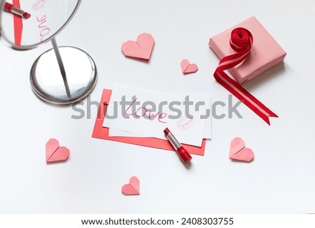 Red paper envelope with white blanks, word love written with red lipstick and pink origami hearts. Valentine's day concept card. Royalty-Free Stock Photo #2408303755