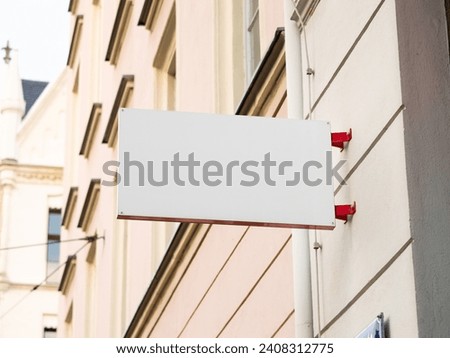 Small store sign template on a house. A white space for a logo or icon. The name of the business or opening hours could be displayed. Signage mock up of a retailer in a town.