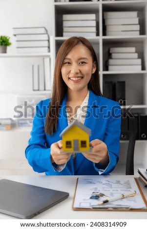 House model near an Asian female sales representative offering prices and conditions of purchase or rental on a table in a new location. In choosing real estate in her office