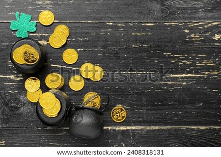Pots with golden coins and paper clover on black wooden background. St. Patrick's Day celebration