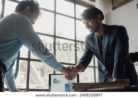 Smiling middle-aged businessman shaking hands with partner making cooperation agreement, business partners meeting in office with laptop and financial documents on table