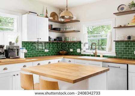 A kitchen detail with butcher block wood countertops, white cabinets, a gold fixture hanging over the island, and green subway tile backsplash. No brands or logos. Royalty-Free Stock Photo #2408342733