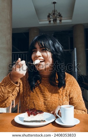 young happy latin woman celebrating happy women's day sitting outside cafe smiling and eating cheesecake, vertical image.