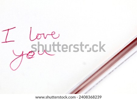 A photo of the saying 'I love you' written on red on a white page beside a red pen. 