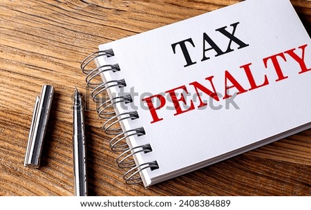 TAX PENALTY text on a notebook with pen on wooden background Royalty-Free Stock Photo #2408384889