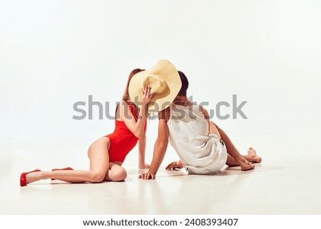 Young people, man and woman in swimwear hiding face behind straw hat against white background. Romance, love. Concept of summer vacation, travelling, retro style, fashion