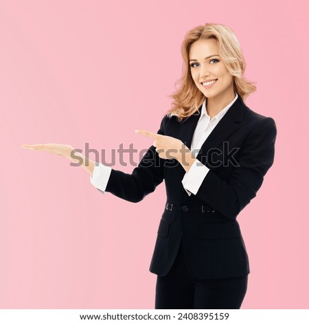 Portrait of smiling businesswoman in confident suit, showing, giving holding something, some product or copy space for text, isolated rose pink background. Square photo.