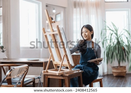 Happy asian woman artist drawing picture on canvas in studio.