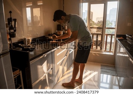 An Indian father grinds whole spices with a mortar and pestle to make masala chai in his kitchen at his home in Mumbai, India. Royalty-Free Stock Photo #2408417379