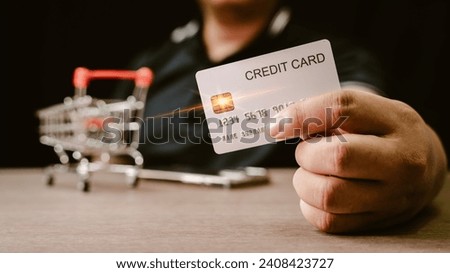 Photograph of a hand holding a credit card And there is a small supermarket cart. Ideas for using a cadet card to shop online or make financial transactions through a cadet card.