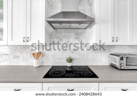 Detail shot of a white luxurious kitchen stove and hood. A marble custom tile back splash is under the white cabinets. Royalty-Free Stock Photo #2408428643