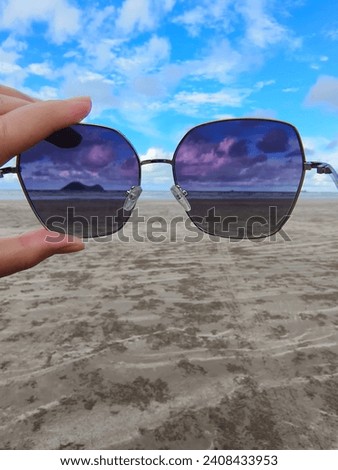 Picture of holding sunglasses with a beautiful beach view. The weather is hot, the sky so bright and the sand is brownies.