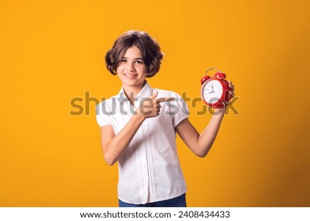 Child girl holds an alarm clock in hand and pointing at it. The concept of education, school, deadlines, time to study