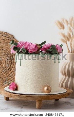 Anniversary cake with white chocolate velvet coating decorated with pink roses on the wooden stand
