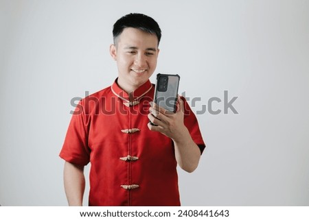 Smile face of Asian man wearing Chinese traditional cloth or Cheongsam while looking at his smartphone on white background Royalty-Free Stock Photo #2408441643