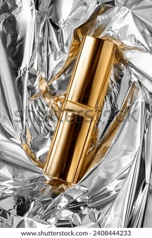 Golden lipstick cover lying on crumpled silver foil background