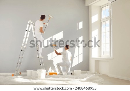 Two male workers from the professional home renovation service painting walls light gray in a big bright living room interior inside a new modern house or apartment Royalty-Free Stock Photo #2408468955