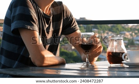 Young man drinking red wine on a terrace of cafe at sunset. Blurred view of European town on the background