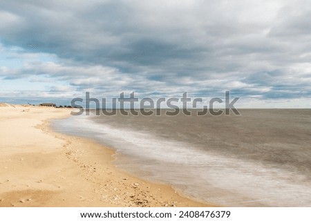 Landscape photo of Hammonasset Beach State Park in Madison, Connecticut. Cloudy sky. Warm tones. Longer exposure time adds some movement to the water. No life pictured in photo.