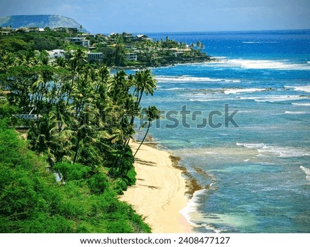 Sandy beach and a blue-green ocean seen from Diamond Head lookout, a high vantage point on the volcanic tuff cone on Oʻahu island. The photo shows the white waves crashing onto the shore, the hill. Royalty-Free Stock Photo #2408477127