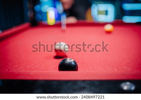 Close-up of billiard balls on red pool table with blurred background, eight ball in focus, player preparing to shoot in the background. Royalty-Free Stock Photo #2408497221