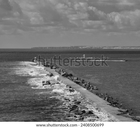 Motor boat entry into the seaport sailing the Arade River in Portimão. Sea waves hitting the protective rocks of the harbor. Black and white photography. Royalty-Free Stock Photo #2408500699