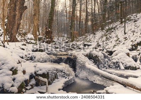 Forest stream in a winter, snowy forest. Ice over water, long shutter speed smoothes out the flow