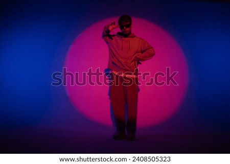 Guy in casual clothes dancing hip hop elements in studio with blue light. Dancer is in red circle of spotlight and demonstrates body plasticity. Full height. Modern street choreography.