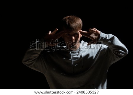 Guy in light street clothes poses on black background of studio. Dancer demonstrates elements of choreography in hip hop style. Modern street dance style.