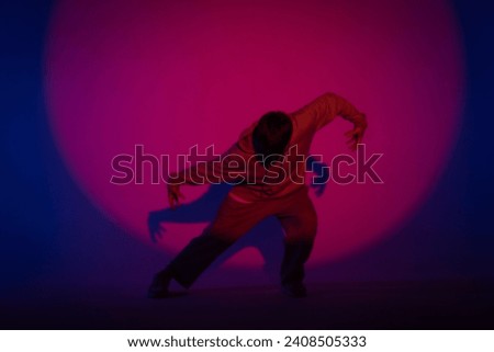 Guy in casual clothes dancing hip hop elements in studio with blue light. Dancer is in red circle of spotlight and demonstrates body plasticity. Full height. Modern street choreography.