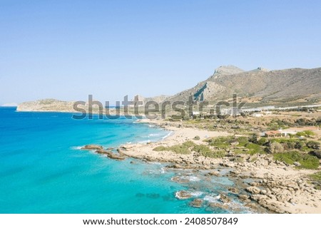 The sandy beach at the foot of the rocky cliffs in the arid countryside , in Europe, Greece, Crete, towards Kissamos, towards Chania, By the Mediterranean Sea, in summer, on a sunny day. Royalty-Free Stock Photo #2408507849