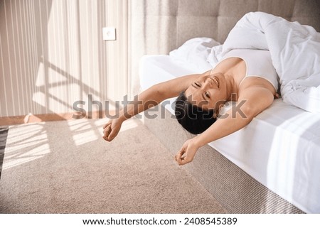 Merry lady enjoying her morning wake-up in cozy bedchamber Royalty-Free Stock Photo #2408545389