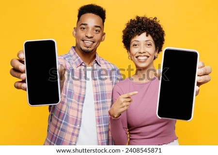 Young couple two friend family man woman of African American ethnicity wear purple casual clothes together hold in hand use show blank screen area mobile cell phone isolated on plain yellow background Royalty-Free Stock Photo #2408545871