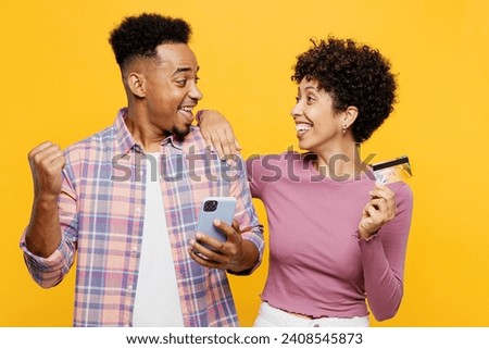 Young couple two friends family man woman wear purple casual clothes together use mobile cell phone hold credit bank card shopping online do winner gesture isolated on plain yellow orange background Royalty-Free Stock Photo #2408545873