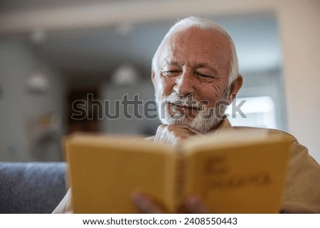 Senior man reading a book in the living room.