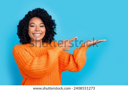 Photo portrait of attractive young woman hold point empty space dressed stylish knitted orange clothes isolated on blue color background