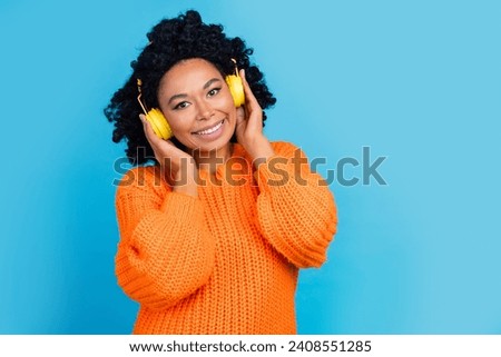 Photo portrait of lovely young lady touch headphones listen music wear trendy knitwear orange garment isolated on blue color background