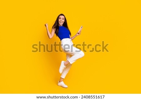 Full length photo of lucky impressed woman wear blue top winning game modern gadget empty space isolated yellow color background