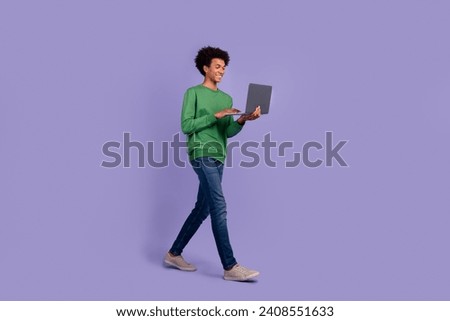 Full length photo of excited funky guy wear green pullover typing message modern gadget walking empty space isolated purple color background