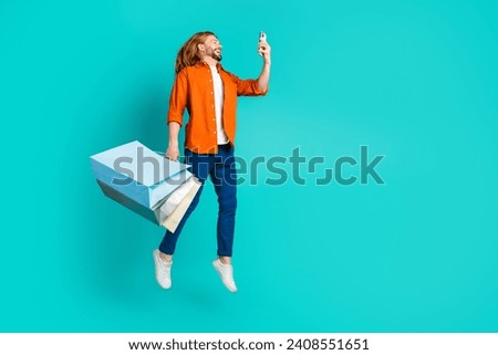 Full size photo of clever guy dressed blue jeans flying hold new clothes look at smartphone isolated on turquoise color background