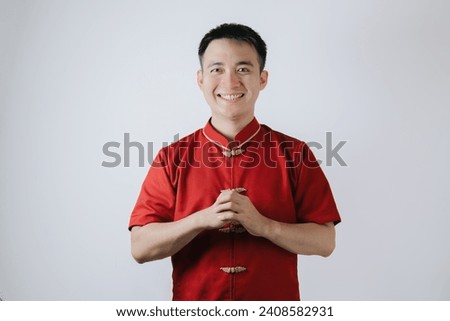 Smile face of Asian man wearing Chinese traditional cloth called Cheongsam with a gesture of congratulations on the Lunar New Year and looking at the camera on white background. Gong Xi Fa Cai. Royalty-Free Stock Photo #2408582931