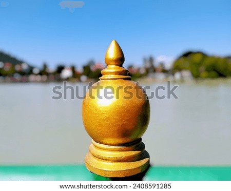The background image is a large reservoir and a blurred image of mountains and houses and the sky in the background. In the center of the image is a beautifully sculpted gold material used to decorate