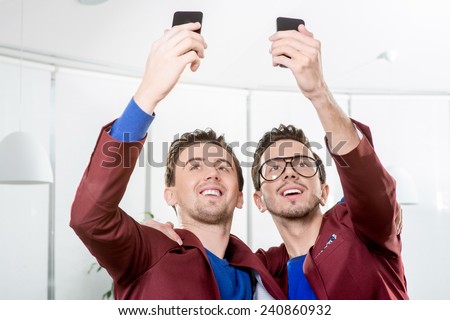 Friendly brothers twins having fun taking selfie photo with smart phone in the white home or restaurant interior